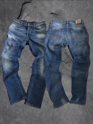 Nudie Jeans Grim Tim blå jeans W34 L34 - Säljer ett par Nudie Jeans Grim Tim i klassisk blå tvätt med slitningar och kontrastsömmar. Modellen har normal passform, raka ben och fem fickor. Materialet är 98% bomull och 2% elastan för lite stretch. Snygga detaljer med Nudie-logga på bakfickan.