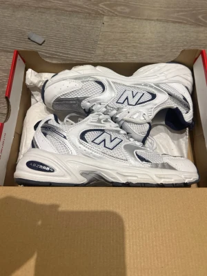 Vita New Balance 530 sneakers - Säljer ett par fräscha New Balance 530 sneakers i vitt med marinblå detaljer. Skorna har meshpaneler för extra andningsförmåga, syntetiska overlays och klassisk snörning. Perfekta för dig som gillar retrovibbar och sportig stil.