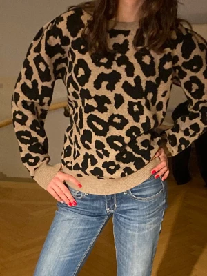 Leopardmönstrad stickad tröja S - Säljer en stickad tröja med svart leopardmönster. Tröjan har rund halsringning, ribbade muddar och lång ärm. Perfekt för dig som vill sticka ut med ett djurmönster i garderoben.🌸Kolla in mina andra annonser!💕