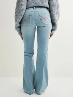 Ljusblå bootcut jeans från Nelly - Säljer ett par ljusblå bootcut jeans med låg midja och snygga rosa broderade detaljer på bakfickorna. Jeansen har dubbla knappar framtill och klassisk femficksdesign. Perfekta för dig som gillar en retro vibe och vill ha ett par jeans som sticker ut lite extra. 💞💞🫰🏻