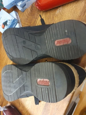 Svarta sneakers med gulddetaljer från Rieker - Snygga svarta sneakers från Rieker med guldfärgade detaljer vid hälen och snörning framtill. Skorna har en platt sula och är tillverkade i syntetmaterial med textilfoder. Perfekta för dig som vill ha en sportig men ändå stilren look.