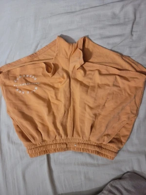 Persikofärgade loose shorts - Säljer ett par persikofärgade shorts från Make New Friends med bred resår i midjan och tryckt text på sidan. De har en loose passform och är perfekta för chill dagar. Materialet är mjuk bomull som känns skönt mot huden.