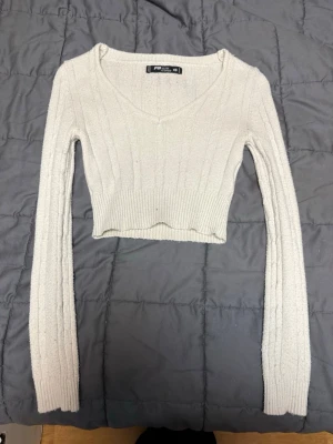 Ljusvit croppad stickad tröja XS - Säljer en ljusvit croppad stickad tröja från FB Sister i storlek XS. Tröjan har v-ringning, ribbade muddar och lång ärm. 
