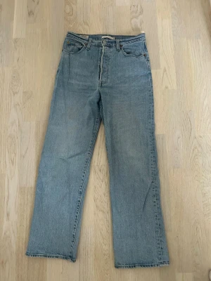 Levi's Ribcage Straight jeans ljusblå - Ljusblå Levi's Ribcage Straight jeans med klassisk femficksmodell och raka ben. Hög midja och snygg vintagekänsla. Tillverkade i slitstarkt jeansmaterial med silverfärgade nitar och knapp. Perfekta för en avslappnad och trendig look. Storlek: W29 L29
