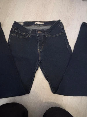 Levi's 715 Bootcut jeans mörkblå - Mörkblå Levi's 715 Bootcut jeans med klassiska kontrastsömmar och femficksdesign. Byxorna har bootcut-ben och är tillverkade i stretchigt jeansmaterial. Levi's Premium-märke bak i midjan och röd Levi's-tag på bakfickan. Den har sina skavanker, en vit färgfläck på knäet (se bild). Pris går att diskutera