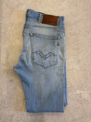 Replay ljusblå skinny jeans herr med slitningar - Säljer ett par ljusblå Replay jondrill jeans med skinny passform. Jeansen har slitna detaljer och hål på benen för en riktigt trendig look. Klassisk femficksmodell med Replay-logga på bakfickan och patch i läder bak i midjan. Perfekta för alla årstider.