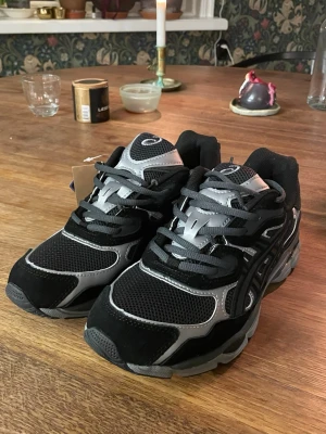 Svarta Asics Gel NYC - Säljer ett par svarta och vita Asics sneakers med coola detaljer och meshpartier för extra andningsförmåga. Säljer på grund av att de var för små för mig. Har aldrig används och är därför i helt nytt skick. Skorna har inga defekter alls. Skriv gärna till mig angående funderingar om skorna. 🤩👍