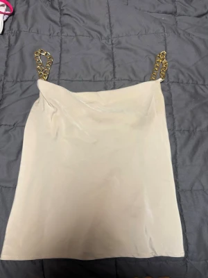 Beige linnetopp med guldkedjor Amisu XS - Säljer en beige linnetopp från Amisu i storlek XS. Toppen har tunna axelband i guldfärgad kedja som ger en snygg detalj. Materialet är slätt och har en lätt glansig finish.