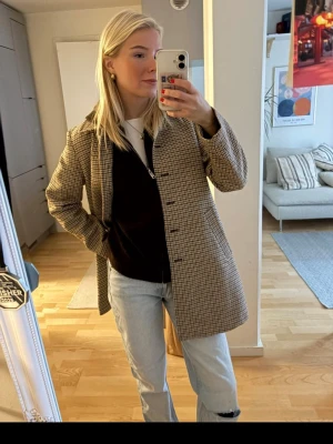 Rutig beige rock med knappar - Säljer en snygg rutig rock i beige och bruna toner. Jackan har klassisk krage, knäppning framtill med knappar och två fickor. Perfekt för dig som gillar en stilren och tidlös look. Passar till både jeans och kostymbyxor.
