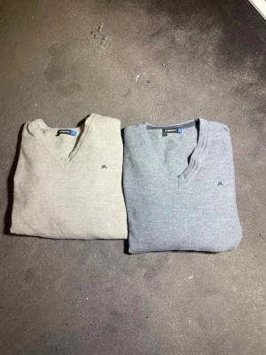 J.Lindeberg V-ringad stickade tröjor - Två stilrena v-ringade stickade tröjor från J.Lindeberg i storlek M. En i ljusbeige och en i grått, båda med diskret broderad logga på bröstet. Perfekta till lager på lager och riktigt sköna material som känns lyxiga. Ska sägas att dom har krympt i tvätten så är för dig som har storlek 130-140 ungefär.