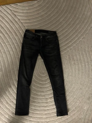 Dondup George Mörkgrå/Svart - Säljer ett par svarta Dondup George jeans i storlek 31 med lätt tvättade detaljer och klassisk femficksdesign. Jeansen har smal passform och är tillverkade i stretchigt jeansmaterial för extra komfort. Perfekta till sneakers eller boots.