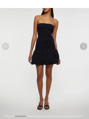 Svart axelbandslös kortklänning Wakakuu - Supersnygg svart axelbandslös kortklänning från Wakakuu. Klänningen har en figurnära överdel och en voluminös, puffig kjol. Perfekt för dig som vill ha en stilren men ändå statement look. Tillverkad i ett mjukt material som sitter bekvämt. Nypris: 1499kr👗🦚🫧🖤