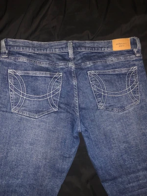 Blå low waisted bootcut jeans från Gina Tricot  - Säljer ett par blå lowwaisted bootcut jeans från Gina Tricot i storlek 44. Jeansen har snygga kontrastsömmar på bakfickorna och klassisk femficksmodell. Jeans är klippta längst benen eftersom de var för långa. Innerbens längden är 75cm. Jeansen har använts 2 gånger. Meddela mig vid frågor, priset kan diskuteras!💕