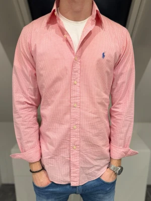 Rosa rutig skjorta från Ralph Lauren - Vi säljer en klassisk rosa skjorta från Ralph Lauren med smått rutigt mönster och blå logga broderad på bröstet. Skjortan har lång ärm, knappar framtill och är tillverkad i bomull. Perfekt till jeans för en clean och fräsch look. Storlek S och säljer den för endast 349kr men kan gå ner vid snabb och smidig affär💙💯 Skicket är 10/10. Hör av er vid frågor! // studio II Resell 