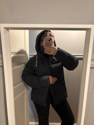 Svart pufferjacka med huva - Säljer en svart pufferjacka, lite likande fjällräven, från peak performance med huva och dragsko. Jackan har dragkedja framtill och är vadderad för extra värme. Insidan har ett mönster med små fjädrar och flera innerfack.  Perfekt för kalla dagar.