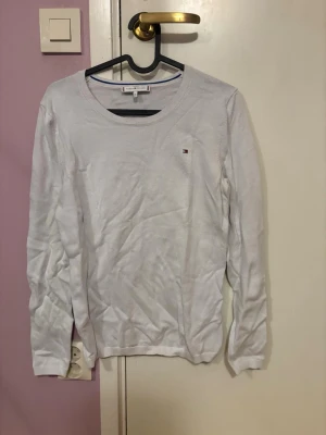 Vit långärmad tröja Tommy Hilfiger - Klassisk vit långärmad tröja från Tommy Hilfiger med rund halsringning och liten broderad logga på bröstet. Tröjan är i mjuk bomull och har ribbade muddar vid ärmslut och nederkant. Perfekt till en clean och enkel stil.