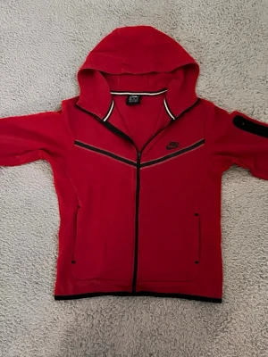 Röd Nike tech - Jag säljer en röd Nike tech hoodie den är i bra skick och använts ett fåtal gånger