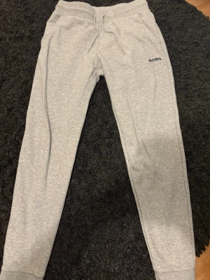 Grå mjukisbyxor från BORG - Snygga ljusgrå mjukisbyxor från BORG med dragsko i midjan och ribbade muddar vid bensluten. Byxorna har en enkel och clean look med diskret logga på ena benet. Perfekta för chill dagar eller träning.