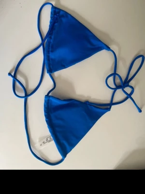 Blå trekantsbikinitopp med knyt - Snygg blå trekantsbikinitopp med tunna knytband både i nacken och runt ryggen. Enkel och stilren design som passar perfekt till stranden eller poolen. Materialet är mjukt och följsamt för en bekväm känsla. De är storlek M men är mer som xs/s