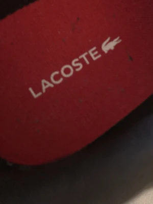 Svarta sneakers från Lacoste - Säljer ett par svarta Lacoste sneakers i skinn med klassisk vit sula och grönt krokodilmärke på sidan. Skorna har snörning och röd innersula med Lacoste-logga. Perfekta för dig som gillar stilrena och sportiga skor. Inget fel på skorna vill bara inte ha dem ! 