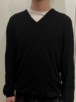 Svart v-ringad tröja J.Lindeberg - Svart v-ringad tröja från J.Lindeberg i storlek XXL. Tröjan har långa ärmar och bruna mockadetaljer på armbågarna. Tillverkad i mjukt merinoull , perfekt för lager på lager under höst och vinter.