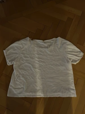 Vit loose t-shirt från SLVN - Vit t-shirt från SLVN med loose passform och korta ärmar. Tryckt etikett med textdetaljer nere till vänster framtill.  Har en bred, avslappnad halsringning som är lite sliten men syns knappt