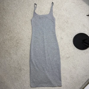 Grå ribbad klänning från Zara Trafaluc - Säljer en enkel och stilren grå klänning från Zara Trafaluc. Klänningen är ärmlös med smala axelband och har en kroppsnära passform som framhäver siluetten. Perfekt till sommaren och lätt att styla med sneakers eller sandaler.