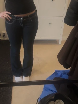 Mörkblå bootcut jeans med vita sömmar - Säljer ett par mörkblå jeans med bootcut passform och vita kontrastsömmar. Byxorna har även låg midja. 