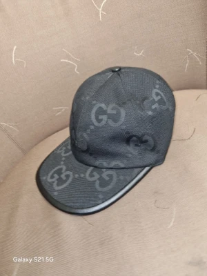 Svart Gucci keps med GG-mönster - Säljer en svart keps från Gucci med det klassiska GG-mönstret över hela kepsen. Kepsen har justerbart band bak i skinn och är tillverkad i slitstarkt tyg. Snygg och stilren accessoar för dig som gillar exklusiva detaljer.