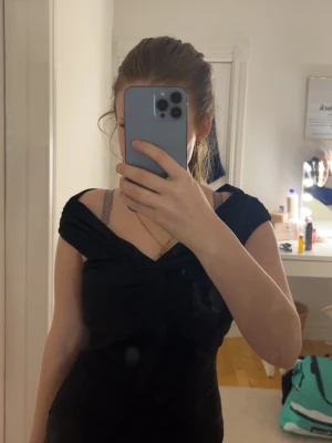 Svart omlott topp från BikBok XS - Säljer en svart omlott topp från BikBok i storlek XS. Toppen har en snygg twistad detalj framtill och breda axelband som ger en offshoulder-look. Materialet är mjukt och stretchigt, perfekt för att skapa en stilren outfit.