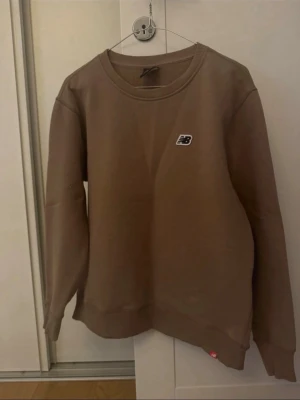 Brun sweatshirt från New Balance M - Säljer en brun sweatshirt från New Balance i storlek M. Tröjan har rund halsringning, ribbade muddar och en liten NB-logga på bröstet. Tillverkad i mjukt bomullsmaterial, perfekt för chill dagar eller när du vill ha en clean look. Har en liten fläck det är därför priset. Pris kan diskuteras!😉