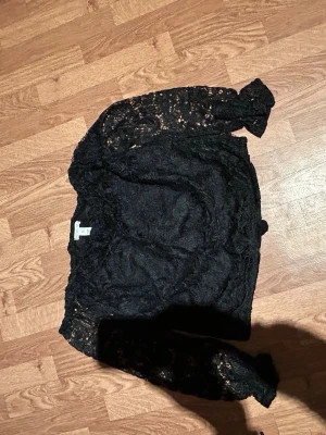 Svart spetsblus med lång ärm - Säljer en svart blus från Monki i storlek S. Blusen är helt i spets med lång ärm och har en elegant, transparent look. Perfekt för dig som vill ha något extra till outfiten. Supersnygg att styla med både jeans och kjol.