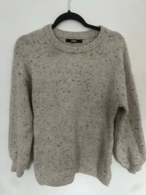 Beige/ljusgrå stickad tröja från BikBok - Mysig stickad tröja från BikBok i storlek S. Tröjan har ett diskret melerat mönster med små prickar i grått och svart, rund halsringning och långa ärmar med ribbade muddar. Perfekt för lager på lager under kyliga dagar.