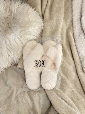 Fluffiga vita tofflor - Supermjuka och fluffiga tofflor i vit/creme färg. Helt nya och oanvända, ligger kvar i originalförpackning. Perfekta för mys hemma, kalla golv eller som present ✨ Storlek 38-40  Mjukt teddy/fuskpälsmaterial Bekväma och varma Stilrena i neutral färg  Säljs pågrund av kommer ej till användning.  Skick:Ny med etikett / i originalförpackning  Färg :Vit / creme 