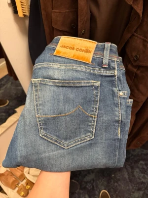 Jacob Cohen jeans - Säljer ett par klassiska blå jeans från Jacob Cohen med snygga kontrastsömmar och detaljer som broderad J på myntfickan och läderpatch bak. Jeansen har rak passform, knappgylf och coolt mönstrat innerfoder. Perfekta till sneakers eller boots.