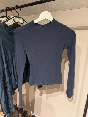 Mörkblå topp från Skims - En enkel och stilren mörkblå långärmad topp i stretchig bomullsblandning. Modellen är figurnära med rund halsringning och passar perfekt till jeans eller kjol. Tillverkad i 98% bomull och 2% elastan för en bekväm känsla. Från Skims