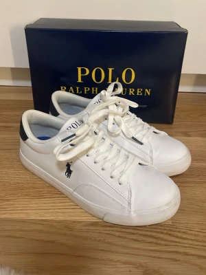 Vita sneakers Polo Ralph Lauren - Snygga vita sneakers från Polo Ralph Lauren med marinblå detaljer och klassisk logga på sidan. Dom är använda en gång men kände sedan attt dom var förstora. Väldigt små i modellen då jag har S37 och passade i S39. Skorna har snörning och är tillverkade i slätt syntetmaterial med rund tå och platt sula. Perfekta till jeans eller shorts för en clean och fräsch look.Kan diskutera priset!😇
