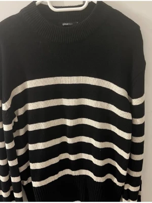 Randig svartvit stickad tröja Gina Tricot - Säljer en svart stickad tröja från Gina Tricot med vita horisontella ränder. Tröjan har rund halsringning, långa ärmar och en relaxed fit. Perfekt för lager-på-lager och passar till både jeans och kjol.