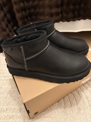 UGGs - UGG Classic Ultra Mini boots i svart skinn med rund tå och platt sula. Insidan är fodrad med mjuk päls för extra värme. Snygga kontrastsömmar och dragflik bak gör dem enkla att ta på. Perfekta för kalla dagar och riktigt cozy vibes. HELT NYA! 