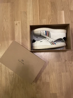 Vita Paul Smith sneakers, strl 43 - Snygga vita Paul Smith sneakers i storlek 43. Skorna är änvända men i ok skick. Ända skadorna är att dom har blivit lagade där bak och har blivit lite slitna där fram. Nypris ca 1700 kr mitt pris endast 399 kr. Fraktar inom 1 dag, om du har någon fundering så är det bara att höra av sig😊