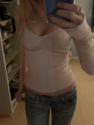 Ljusrosa långärmad topp med v-ringning - Säljer en ljusrosa långärmad topp med v-ringning och rynkdetalj framtill. Toppen är tight i passformen och har tunna, mjuka material som känns sköna mot huden. Perfekt att styla med jeans eller kjol för en enkel men snygg look.
