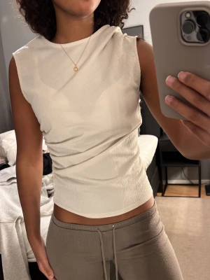 Beige ärmlös topp med drapering - Säljer en stilren Beige topp med draperad effekt och rund vid halsen.