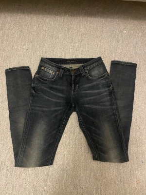 Svarta Nudie Jeans, storlek W27 L34 - Säljer ett par mör blå  jeans från Nudie Jeans med klassisk femficksmodell och snygga slitningar på framsidan. Jeansen har raka ben och subtila kontrastsömmar på bakfickorna. Tillverkade i slitstarkt denimtyg som sitter riktigt bra.
