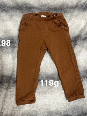 Bruna mjukisbyxor med volangdetalj - Säljer ett par bruna mjukisbyxor med fina volangdetaljer vid fickorna. Byxorna har resår i midjan. Perfekta för en avslappnad och bekväm stil.🌸 Fint använt skick. Storlek 98