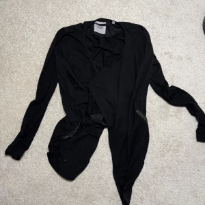 Svart omlottkofta från Object XS - Säljer en svart omlottkofta från Object i storlek XS. Koftan har långa ärmar, asymmetrisk framkant och coola dragkedjedetaljer på sidorna. Perfekt för lager på lager och ger en snygg, avslappnad look.