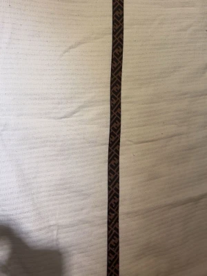 Vit väst med brunt mönsterband - Säljer en vit väst med ett brunt band med grafiskt mönster längs framsidan. Västen har en stilren look och bandet ger en exklusiv touch. Perfekt för dig som vill sticka ut lite extra. Helt nytt!!!