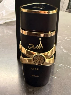 Lattafa Asad Eau de Parfum - Lattafa Asad Eau de Parfum i en snygg svart och guld design. Flaskan rymmer 100 ml och har en unik look som sticker ut i samlingen. Perfekt för dig som vill ha något exklusivt och trendigt.