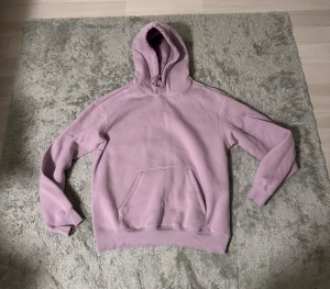 Ljuslila hoodie med huva - Säljer en stilren ljuslila hoodie med huva och klassisk magficka. Tröjan har långa ärmar och ribbade muddar vid ärmslut och nederkant. Perfekt för chill dagar eller när du vill ha en soft look.