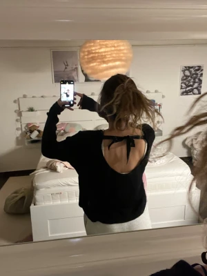 Svart stickad tröja med öppen rygg - Svart stickad tröja från Divided med croppad passform och lång ärm. Tröjan har en öppen rygg med en snygg rosettdetalj upptill. 