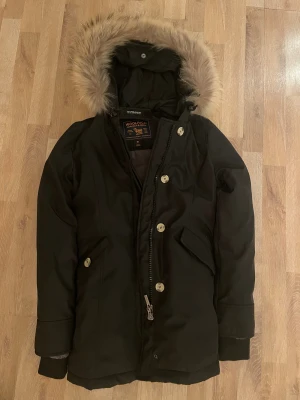 Äkta Woolrich jacka - Säljer en äkta svart Woolrich ( pris kan diskuteras) med huva och snygg pälskant. Jackan har dragkedja och knappar framtill, två stora fickor. Taggarna är perfekta och har bara andvänd den en två gånger 